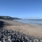 Plage de Pourville-sur-Mer, galets et sable en premier plan, falaises de la Côte d'Albâtre en arrière-plan, ciel bleu