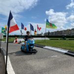Enfant sur une piste de kart en bord de mer à Dieppe, avec drapeaux et front de mer en arrière-plan
