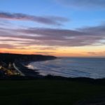Vue sur la baie de Pourville-sur-Mer au coucher de soleil, ciel rose et falaises