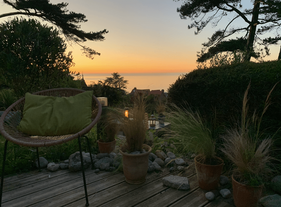 Terrasse aménagée avec fauteuil et plantes face à la mer au coucher du soleil en Normandie