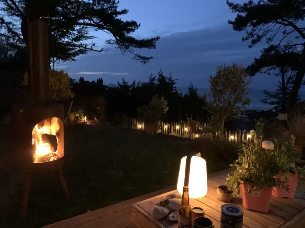 Brasero allumé et lanterne sur la terrasse au crépuscule, le jardin éclairé et la mer en fond