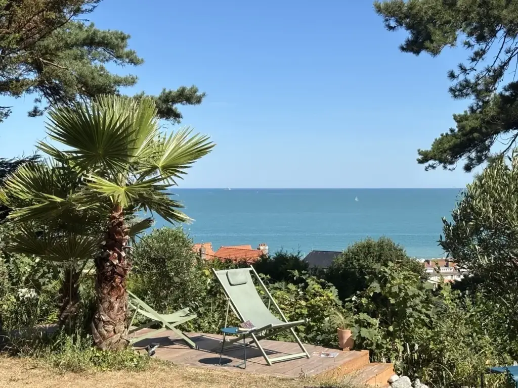 Chiliennes sur le deck à côté d'un palmier, face à la mer turquoise, dans le jardin du Carré Vue Mer à Pourville-sur-Mer