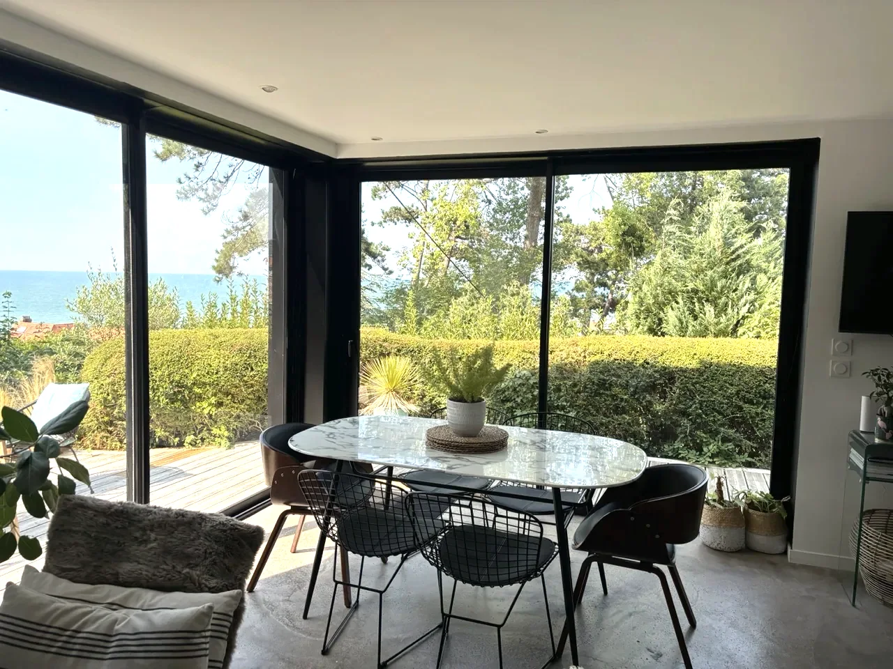 Essbereich mit großem ovalem Tisch vor den Fensterfronten mit Blick auf Garten und Meer