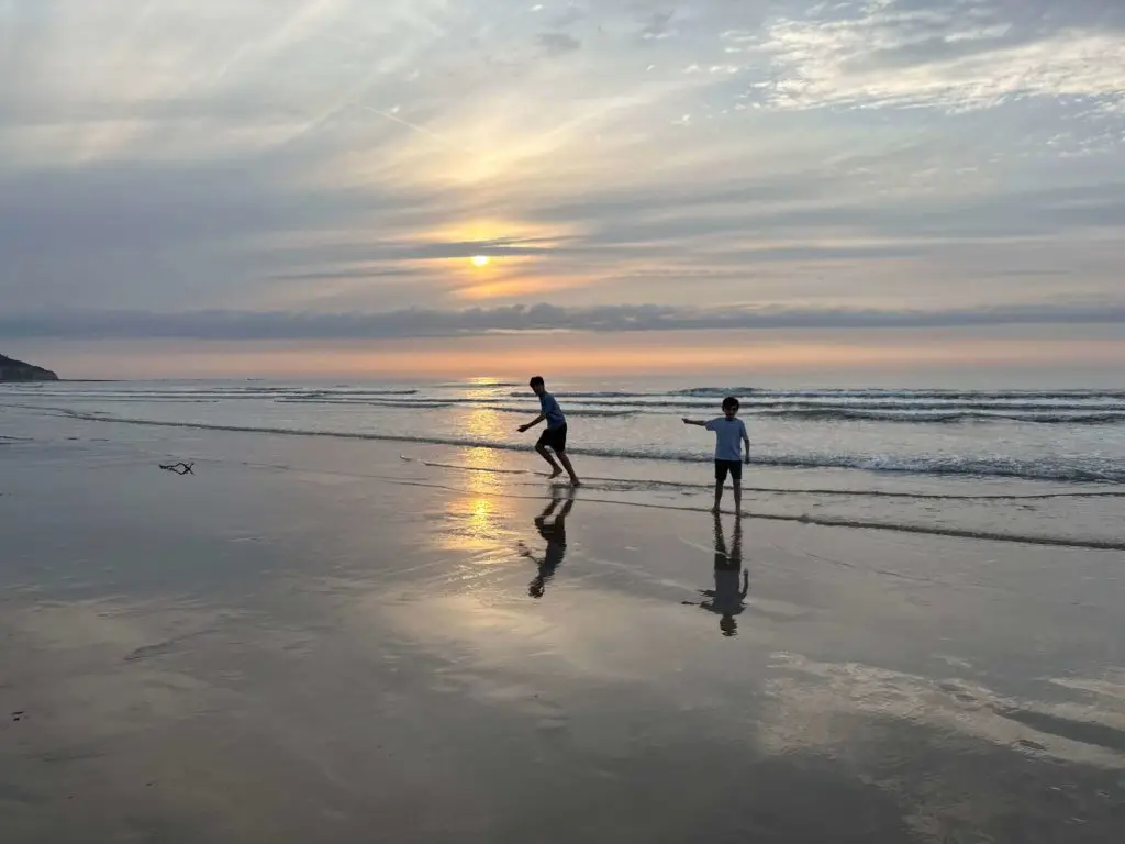 Enfants jouant sur la plage au coucher du soleil à Pourville-sur-Mer en Normandie avec reflets sur le sable
