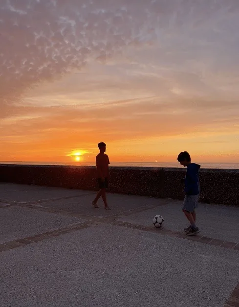 Silhouetten von Kindern beim Ballspielen auf der Strandpromenade bei Sonnenuntergang