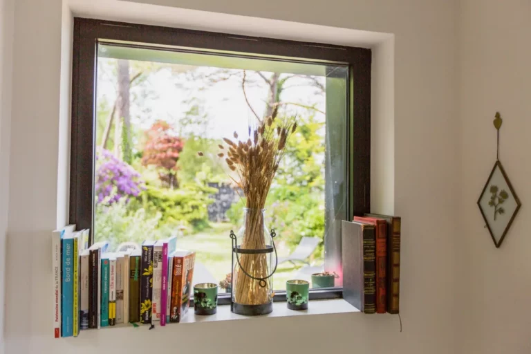 Fensterbank mit Büchern und einem getrockneten Weizenstrauß, mit Blick auf den blühenden Garten