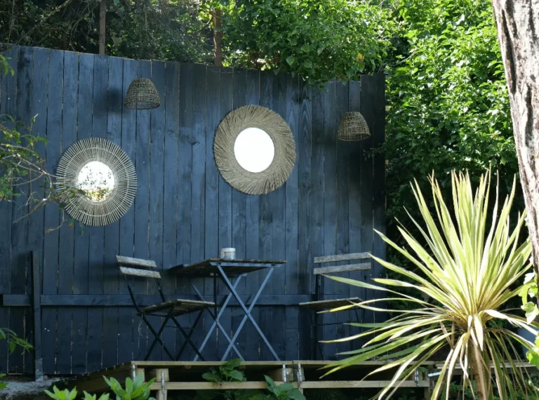 Kleiner Rattanspiegel und blauer Bistrotisch an der schwarzen Fassade, Entspannungsecke im Garten des Carré Vue Mer