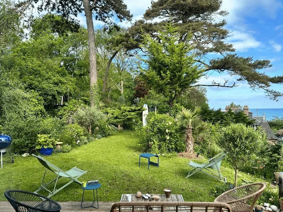 Le jardin en paliers du Carré Vue Mer, pelouse, palmiers et grands pins, avec la mer à l'horizon