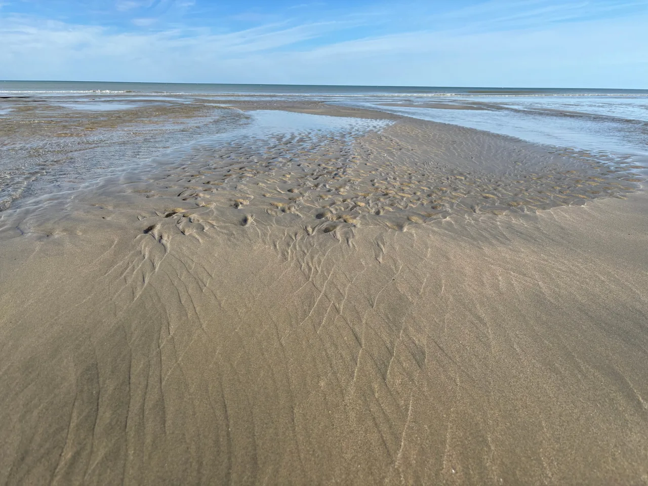 Plage de sable ridé à marée basse à Pourville-sur-Mer, avec des flaques et la mer au loin sous un ciel bleu