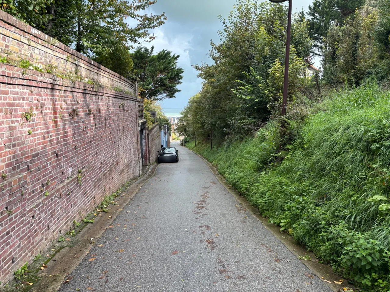 Descente entre les murs de brique Rue en pente le long d'un haut mur de brique, sur le trajet à pied vers la plage de Pourville