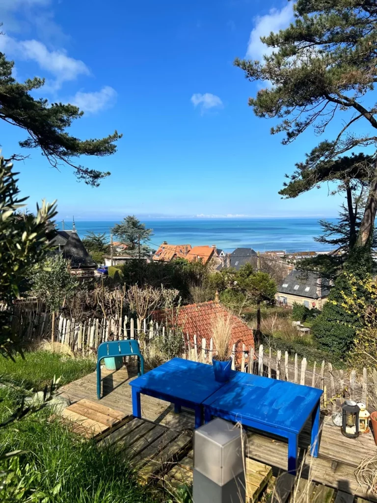 Blaue Beistelltische auf einer kleinen Holzterrasse im Garten mit Blick auf Meer und Dächer von Pourville