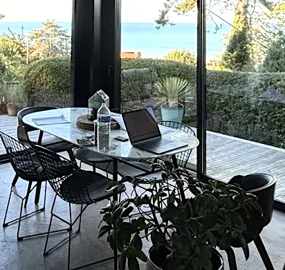 Télétravail face à la mer : ordinateur portable sur la table ovale effet marbre devant les baies vitrées, villa à Pourville