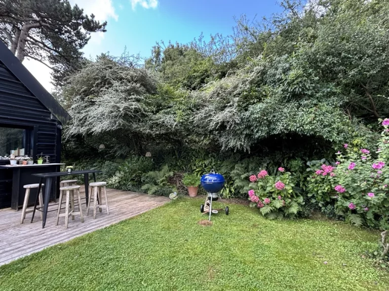 Blauer Grill auf dem Rasen neben dem Stehtisch und den Hockern auf der Terrasse