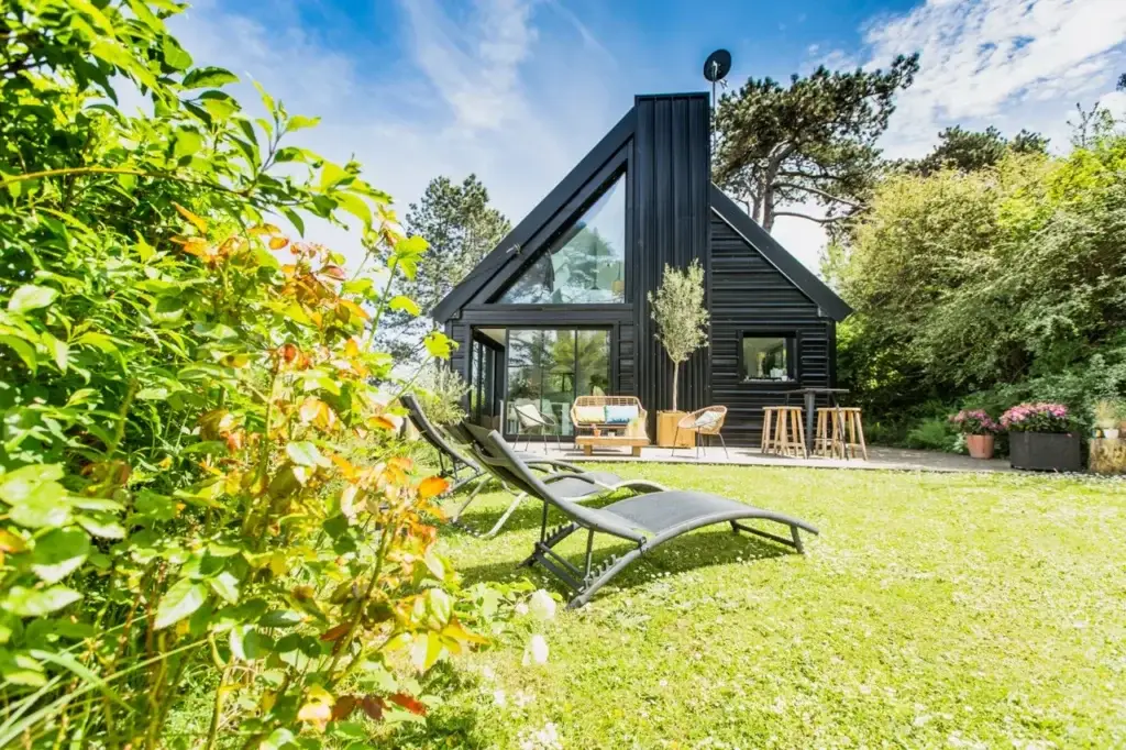 Villa en acier noir avec grande verrière, terrasse et transats sur la pelouse ensoleillée