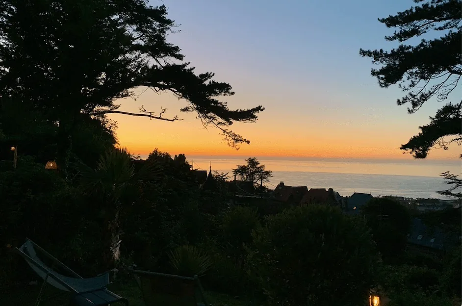Coucher de soleil orangé sur la mer depuis le jardin du Carré Vue Mer, entre les pins, à Pourville-sur-Mer